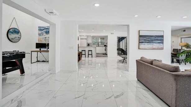 A spacious living area with a marble floor, a foosball table, a grey sofa, and a dining area with a bar. - Luxe Mansion/10min Walk Beach/Gameroom/Heated pool (Hollywood)
