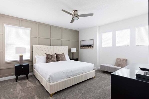 A modern bedroom with a large bed, a ceiling fan, a bedside table, and a desk with a computer. - 4BR Reunion Villa | Theater, Game Room & Pool (Kissimmee)