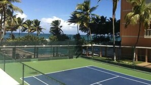 A tennis court with a view of the ocean and palm trees. - Oceanfront on 17th Floor in Condado (San Juan)