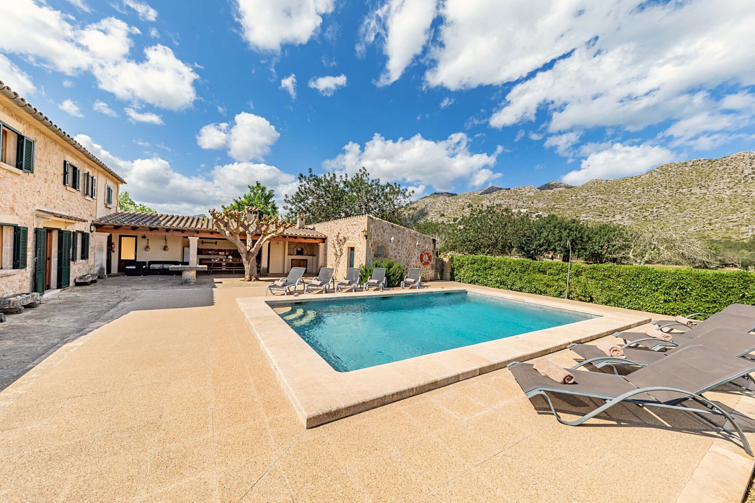 A swimming pool with lounge chairs, a stone building, and a clear sky.
