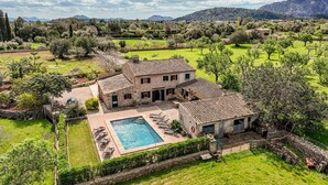 Una villa con piscina, rodeada de vegetación exuberante y montañas al fondo.