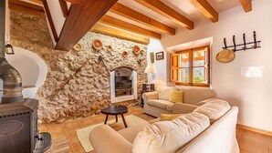 Una sala de estar acogedora con pared de piedra, vigas de madera, chimenea, sofá y ventana con cortinas.
