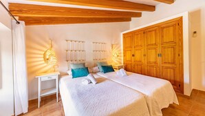 Un dormitorio con una cama grande, vigas de madera en el techo, un armario y lámparas de noche.