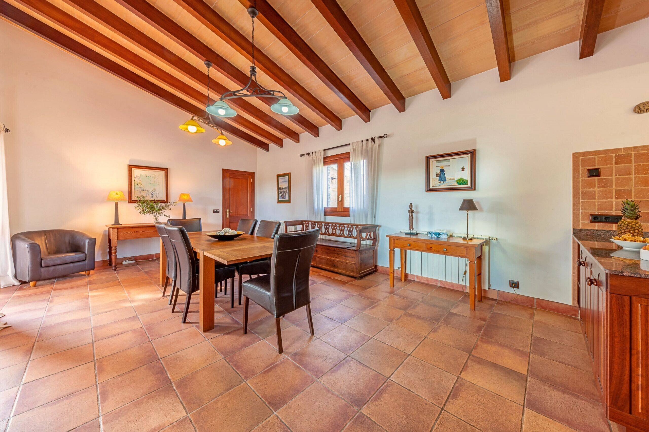 A spacious dining area with a wooden table and chairs, a sofa, and a kitchen area with a tiled backsplash.