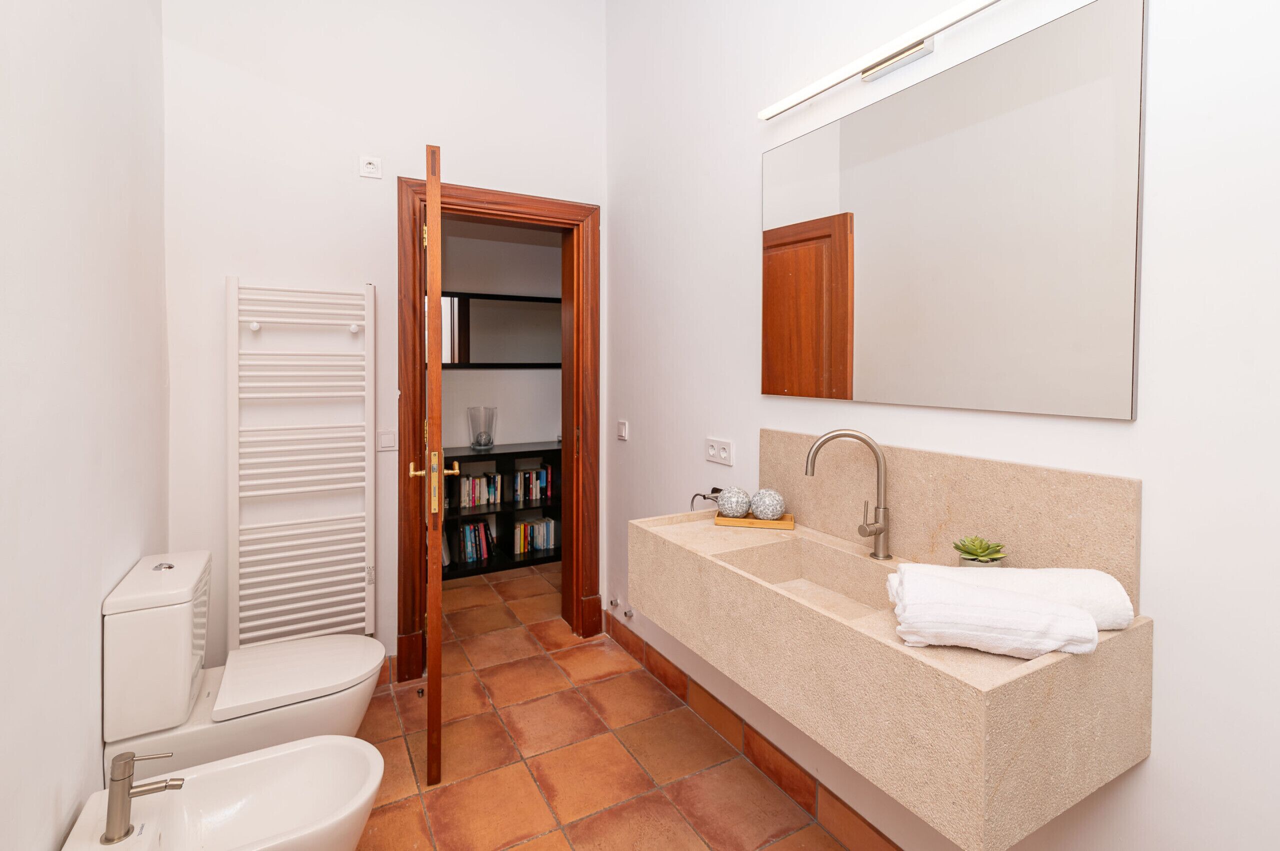 A bathroom with a toilet, sink, and mirror. There is a towel on the sink and a plant on the counter.