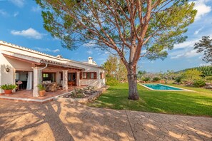 Enjoy a patio with dining set and outdoor furniture, surrounded by a serene lawn and trees, with a swimming pool in the background.