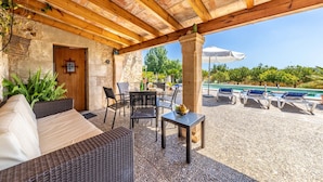 Un patio al aire libre con mobiliario de mimbre, una piscina y un muro de piedra.