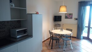 A compact kitchen with a microwave, a dining table with chairs, a hanging lamp, and a TV on the wall. - Casa Maffei PLUS apartment 4, 1st floor, balcony, wonderful lake view, parking (Tignale)