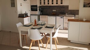 A modern kitchen with white cabinets, a built-in oven, and a dining area with a table set for four. - Superb apartment with port and sea view, large balcony, quiet, free parking, wifi (bandol)