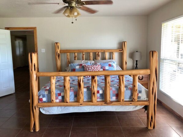 A wooden bed with a quilt, a ceiling fan, and a window with blinds.