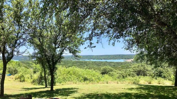 Eine Terrasse mit einer großen Vase, umgeben von üppiger Vegetation und Blick auf einen See.
