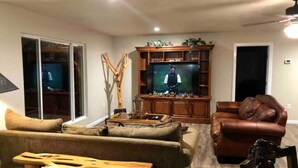 Ein Wohnzimmer mit einem großen Flachbildfernseher, einem braunen Ledersofa, einem Holztisch und einem Holzstuhl.