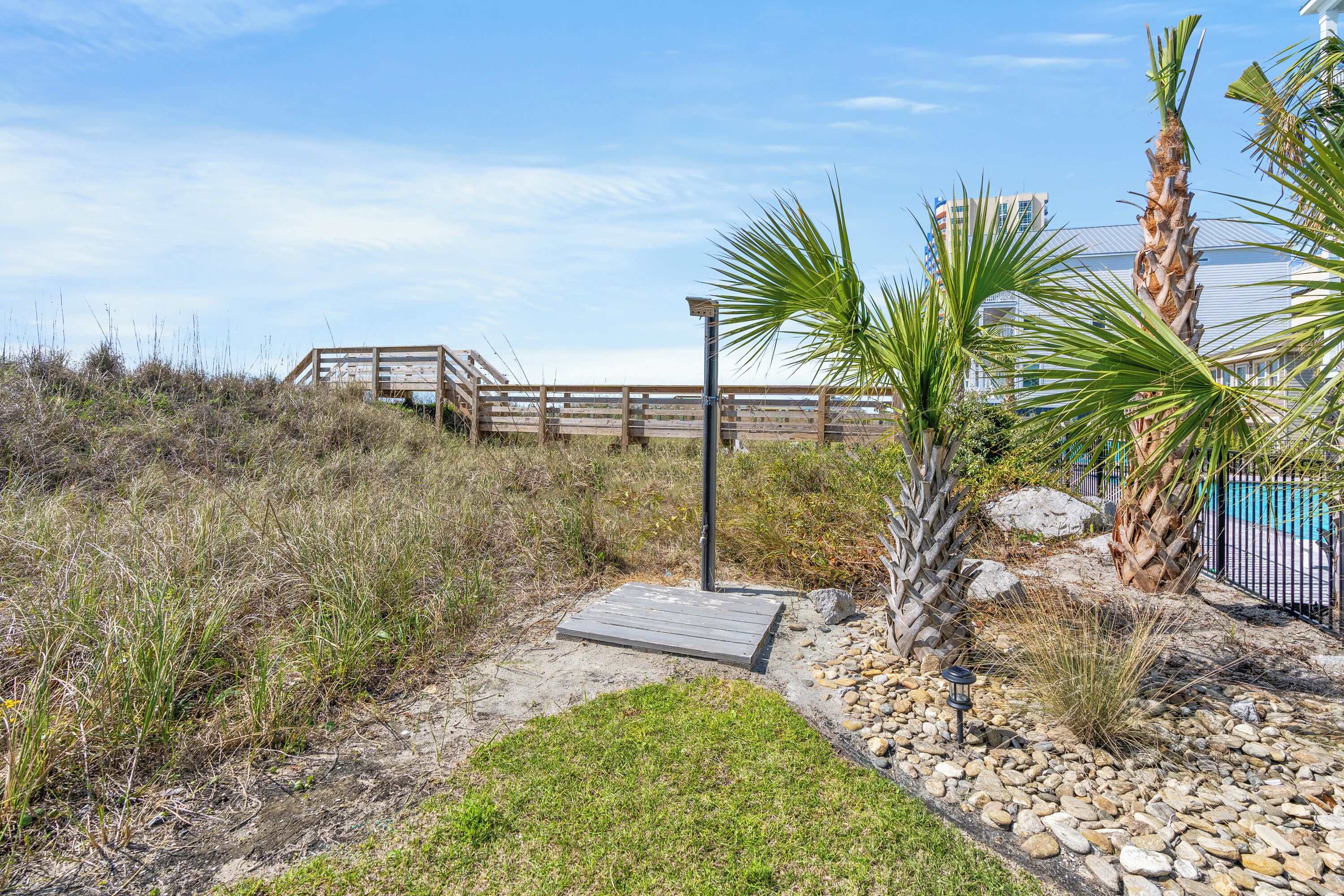 A wooden boardwalk leading to a beach area with a palm tree and a lamp post.