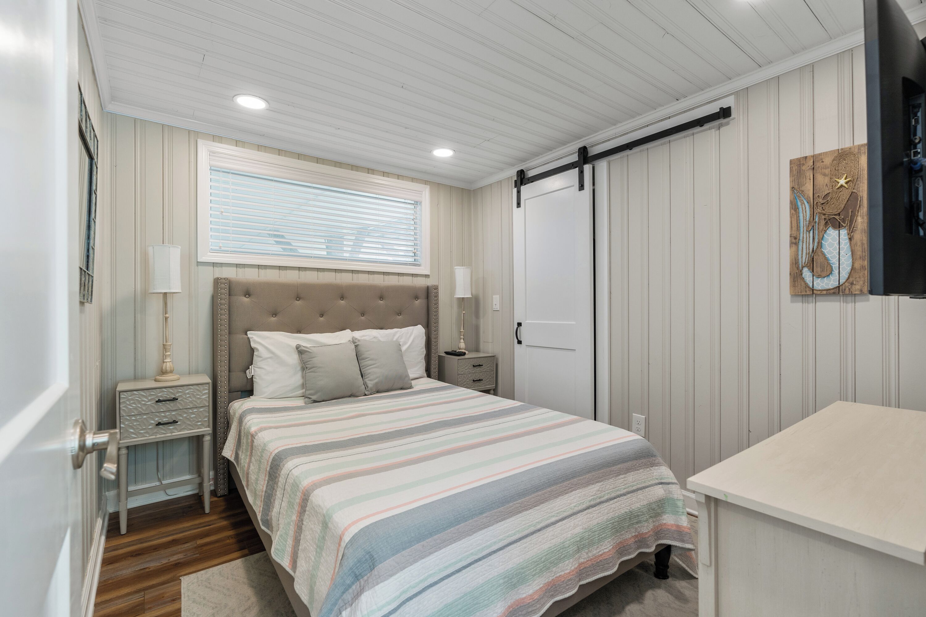 Een slaapkamer met een bed, nachtkastjes, een dressoir, een raam met jaloezieën en een aan de muur hangend kunstwerk.