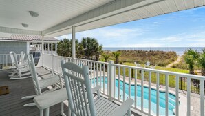 A covered outdoor area with a pool, white rocking chairs, and a view of the ocean.
