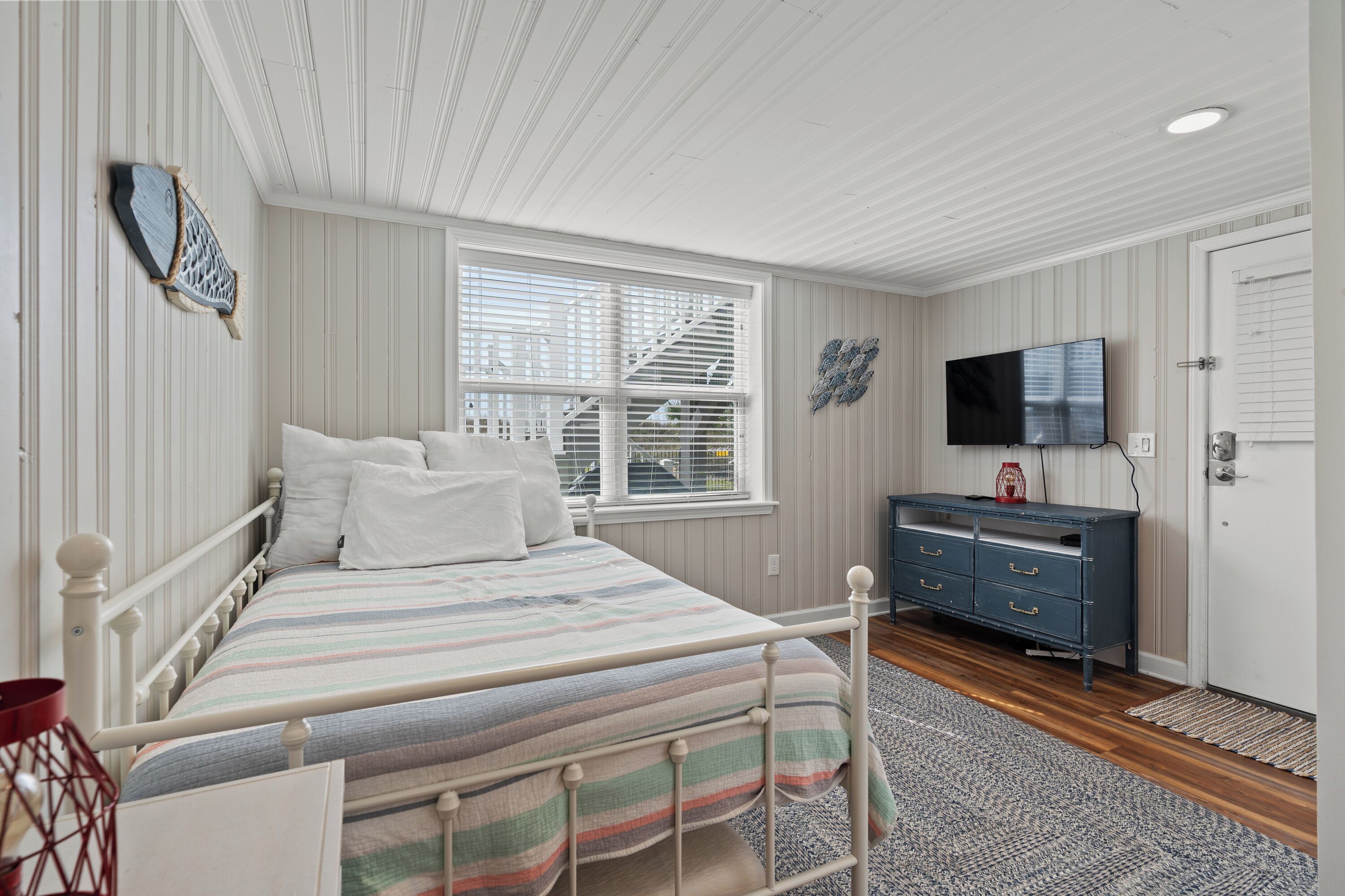 A bedroom with a bed, dresser, TV, and window with blinds.