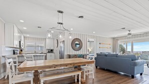 A spacious kitchen with white cabinetry, a wooden dining table, and a gray sofa.