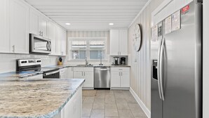 A modern kitchen with white cabinetry, stainless steel appliances, a granite countertop, and a dishwasher.