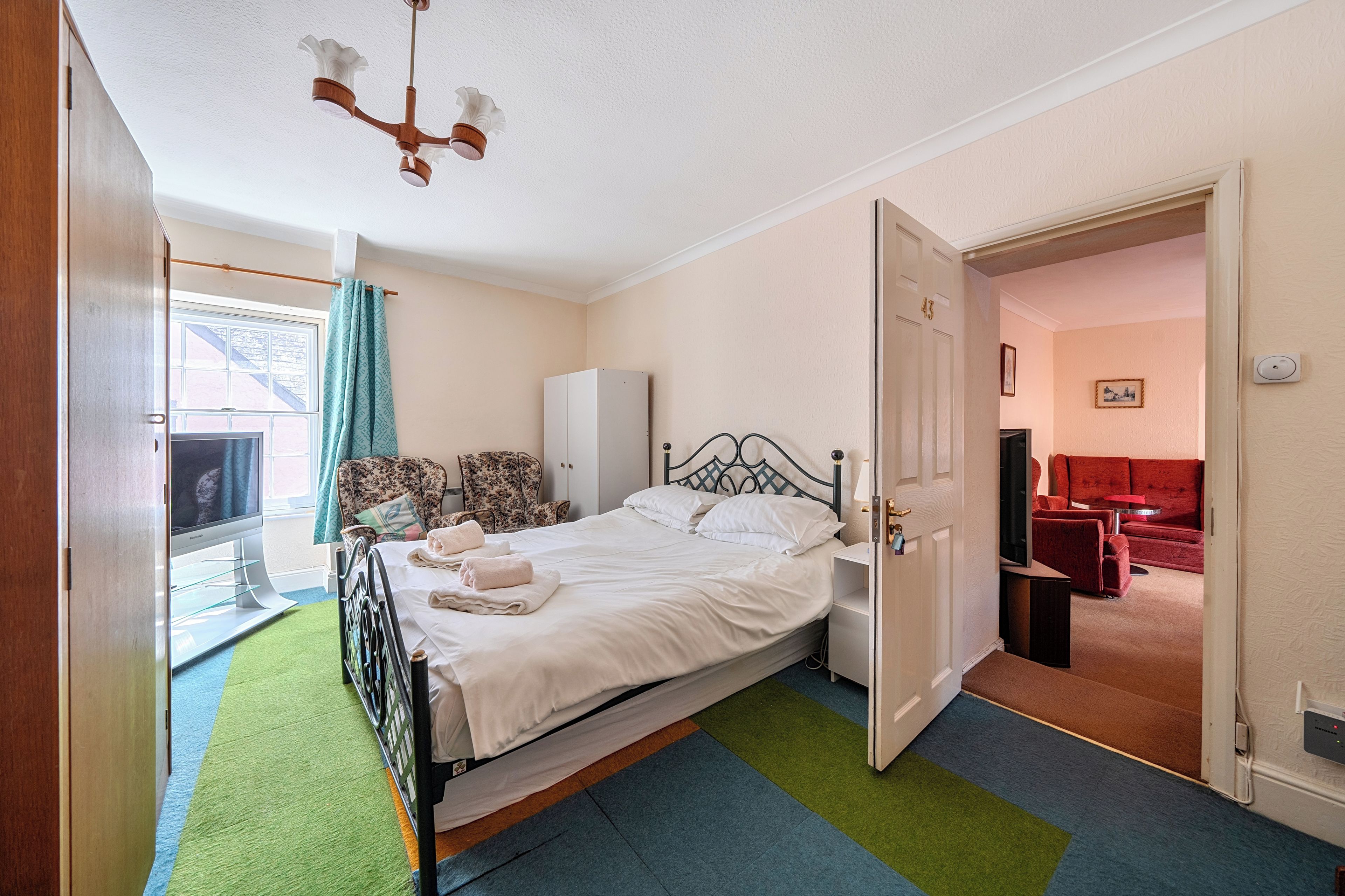 A hotel room with a bed, a wardrobe, a desk, a chair, and a television.