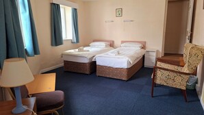 A hotel room with two single beds, a desk with a lamp, a chair, a wardrobe, and a door leading to another room. - House in Historic Village - Sleeps 6 (Minehead)