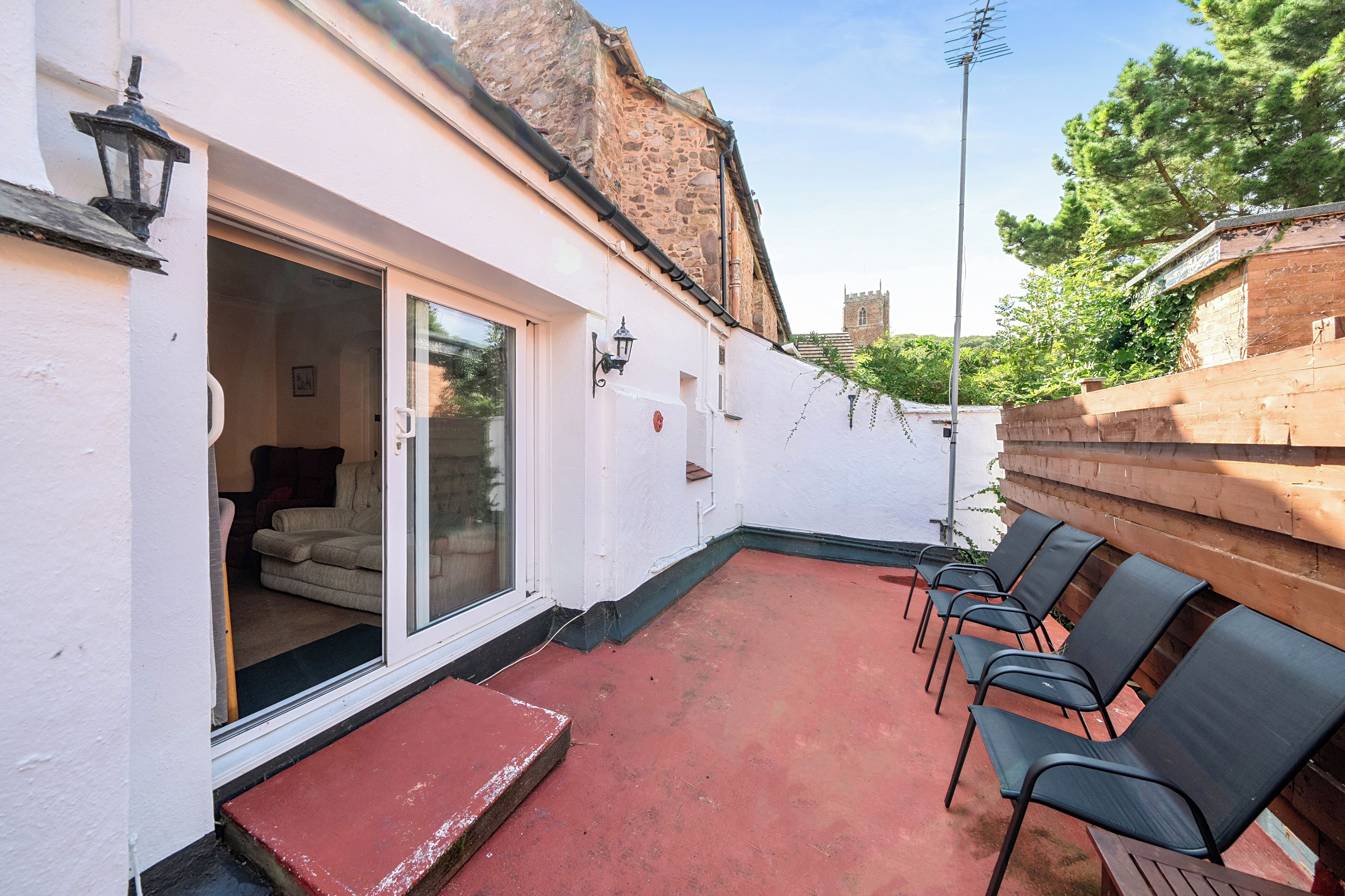 A patio with a red floor, white walls, and a sliding glass door leading to a room with a bed and a chair.