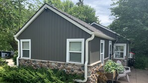 Une maison de plain-pied avec des fondations en pierre, des encadrements de fenêtres blancs et un revêtement extérieur de couleur gris foncé.