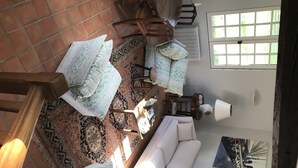 Una amplia sala de estar con un sofá blanco, alfombras estampadas y un comedor con muebles de madera.