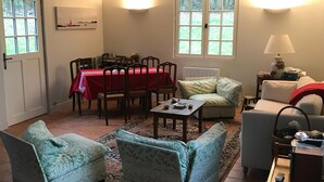 Un salón acogedor con comedor, que incluye un mantel rojo, dos sillones, un sofá y una lámpara.