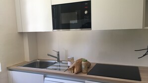 Una cocina compacta con lavavajillas Bosch, un fregadero, un microondas y una encimera con un tarro de pasta y una tabla de cortar.