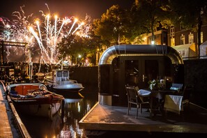 A waterfront restaurant with outdoor seating, a covered area, and boats docked nearby. - The Coon floating home / ecolodge ('s-Hertogenbosch)