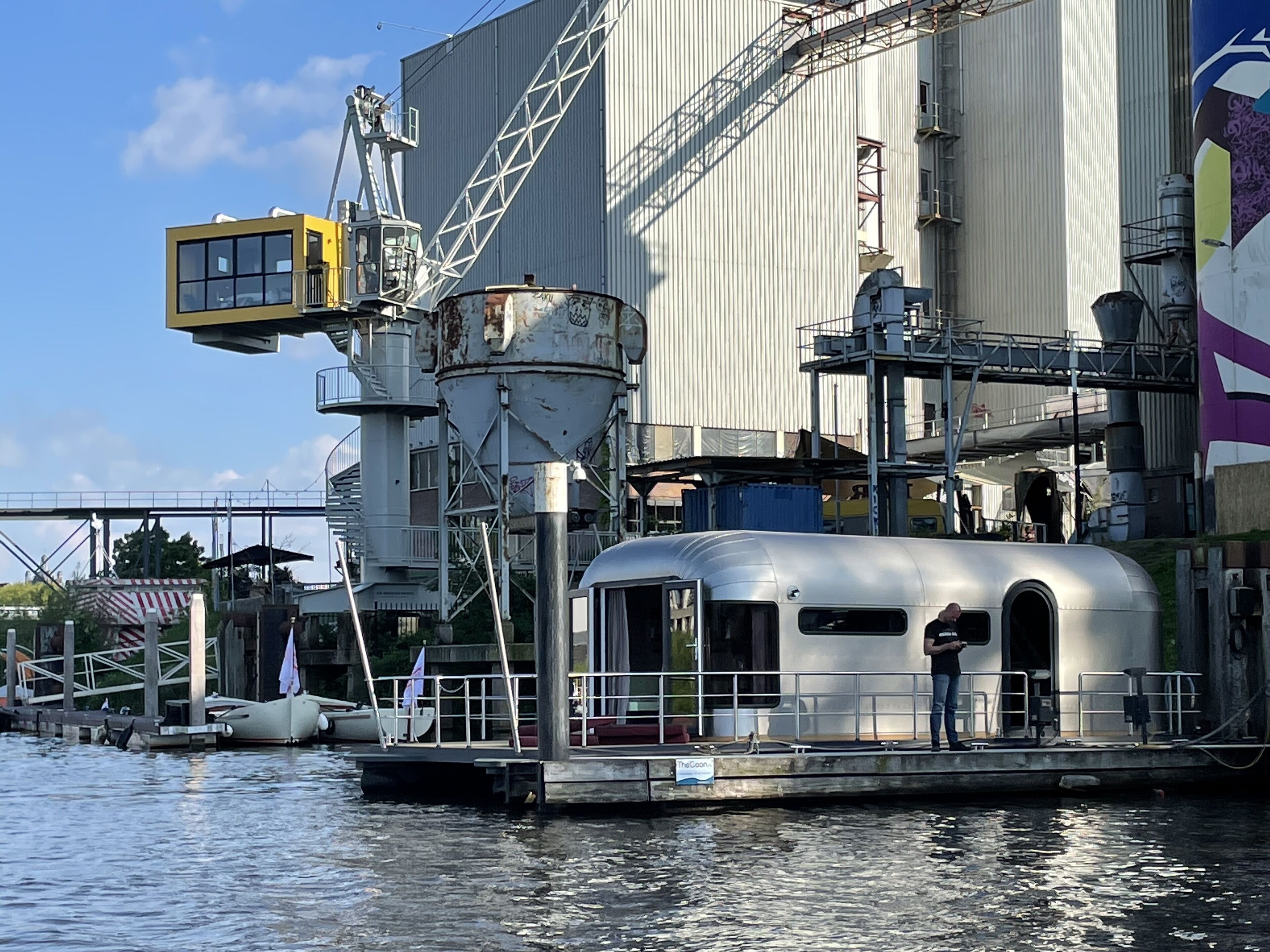 En stilleliggende båd ved et fortøjningsbro med industribygninger i baggrunden.