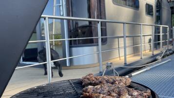 A grill with two steaks cooking, a metal railing, and a silver train in the background.
