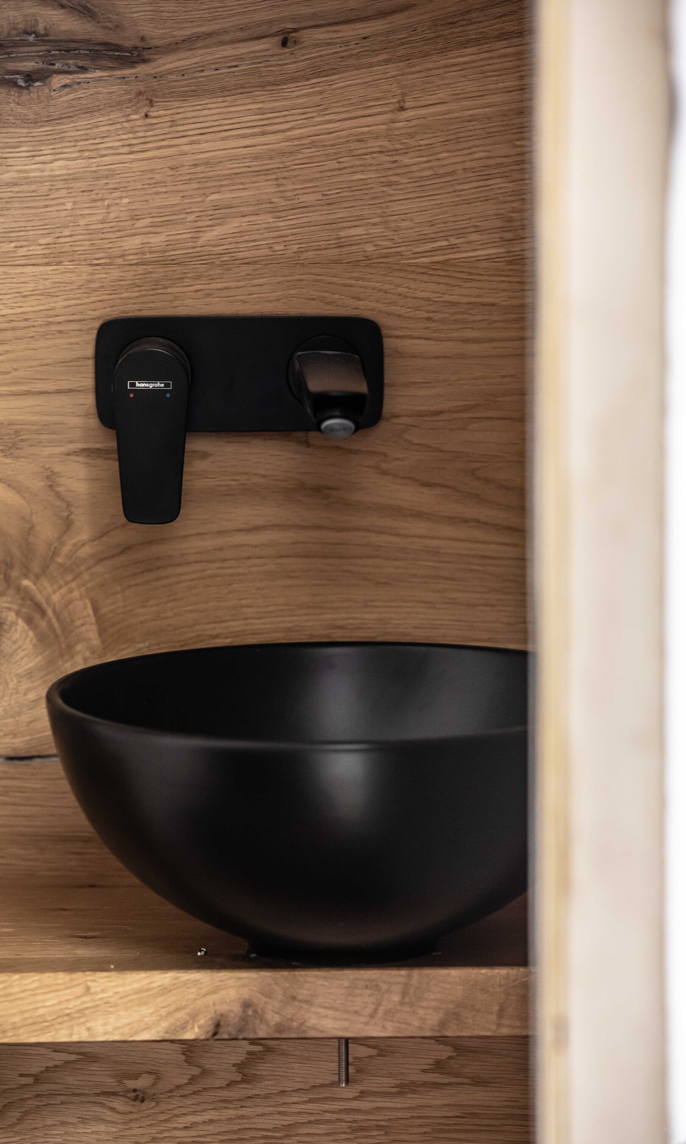 A black bowl on a wooden surface with a black object above it.