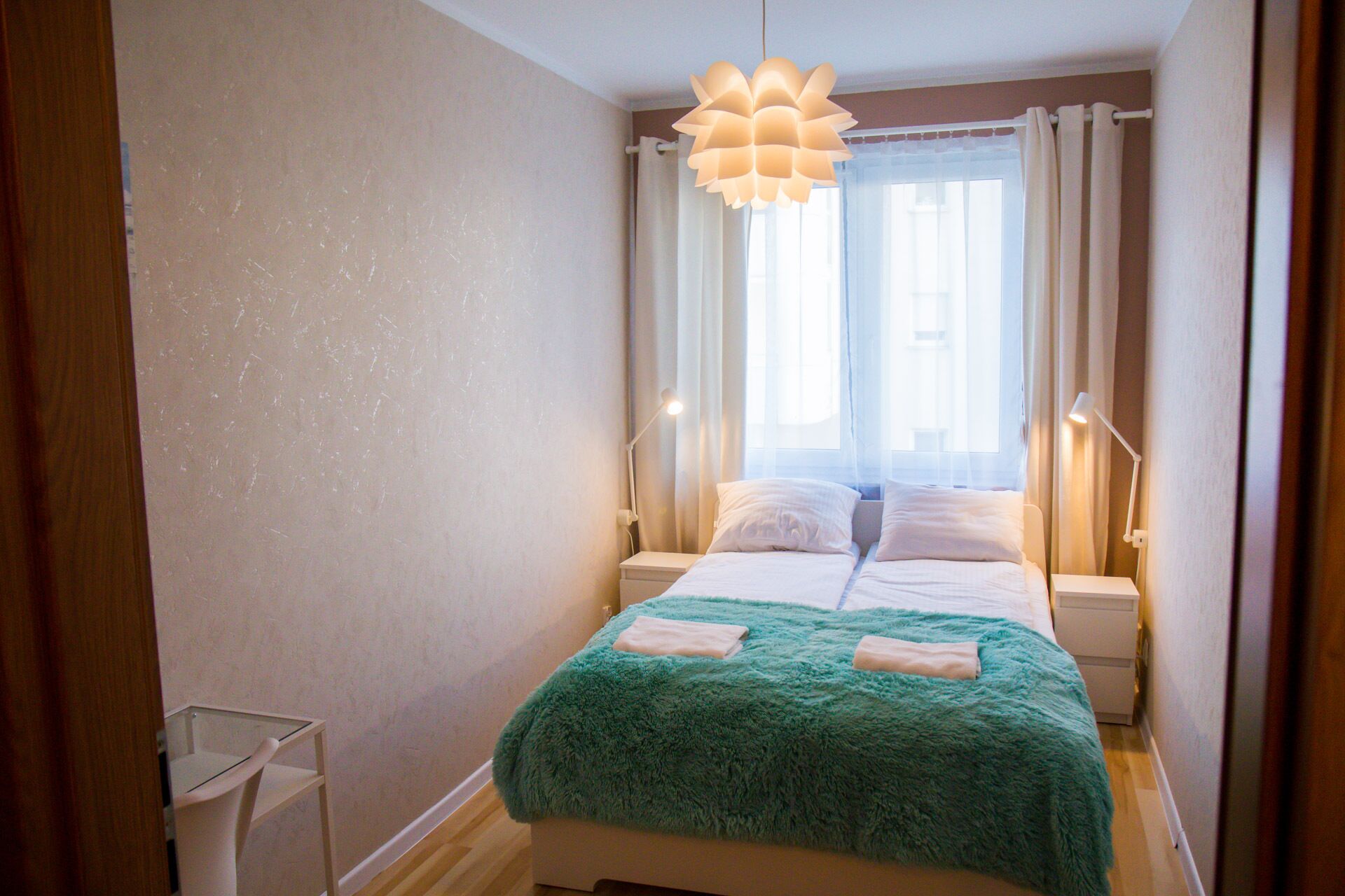 Un dormitorio con cama, ventana con cortinas, lámpara colgante y lámparas de noche.