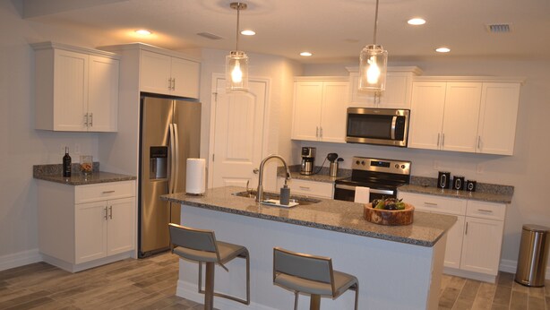 A modern kitchen with white cabinets, stainless steel appliances, and a central island with bar stools. - Brand new heated pool home. (Rotonda West)