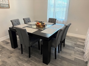 Una mesa de comedor con seis sillas, un frutero y manteles individuales.