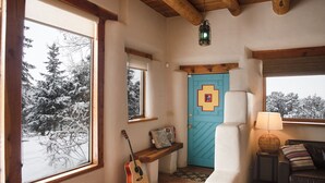 Um quarto acolhedor com teto de madeira, porta azul, um violão encostado na parede e um banco junto à janela.