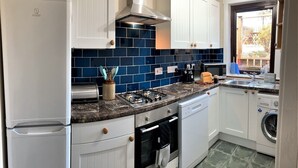 Una cocina con armarios blancos, una estufa a gas, un microondas y una lavadora.
