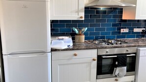 Una cocina con gabinetes blancos, un salpicadero de azulejos azules, una estufa a gas y un horno empotrado.