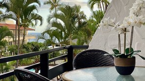 Un balcon avec des fauteuils en osier, une table en verre et une orchidée en pot.