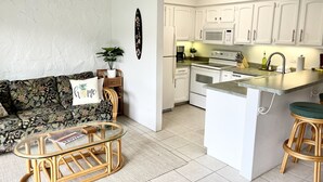 Une cuisine moderne avec des meubles blancs, un îlot central et un coin repas comprenant une table et des chaises en osier.