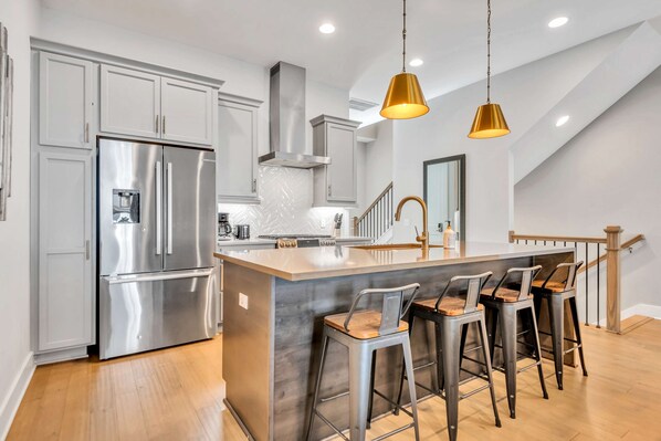 A modern kitchen with stainless steel appliances, a central island with bar stools, and pendant lighting.