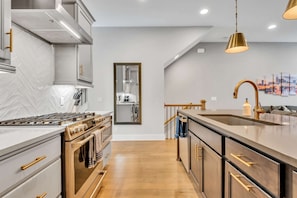 A modern kitchen with a herringbone tile backsplash, stainless steel appliances, and a wooden floor.