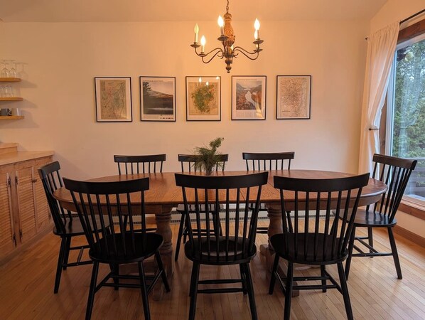 A dining room with a wooden table and chairs, a chandelier, and framed pictures on the wall.