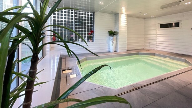 Ein moderner, überdachter Pool mit klarem Wasser, umgeben von gefliestem Boden und weißen Wänden.