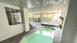 Ein Hallenbad mit Glasveranda, eine Terrasse mit Stühlen und Tisch sowie große Fenster, die viel Tageslicht hereinlassen.