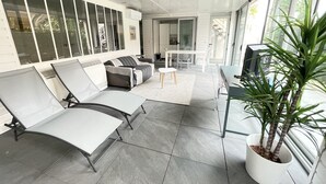 Ein moderner Außenbereich mit einer Couch, zwei Lounge-Stühlen, einem kleinen Tisch und einer Topfpflanze.