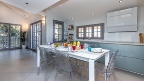 Eine moderne Küche mit Essbereich, mit einem weißen Tisch, transparenten Stühlen, einem großen Fenster und einem eingebauten Backofen.