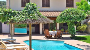 Una piscina con sillas de descanso, una mesa con sillas y una sombrilla de paja.