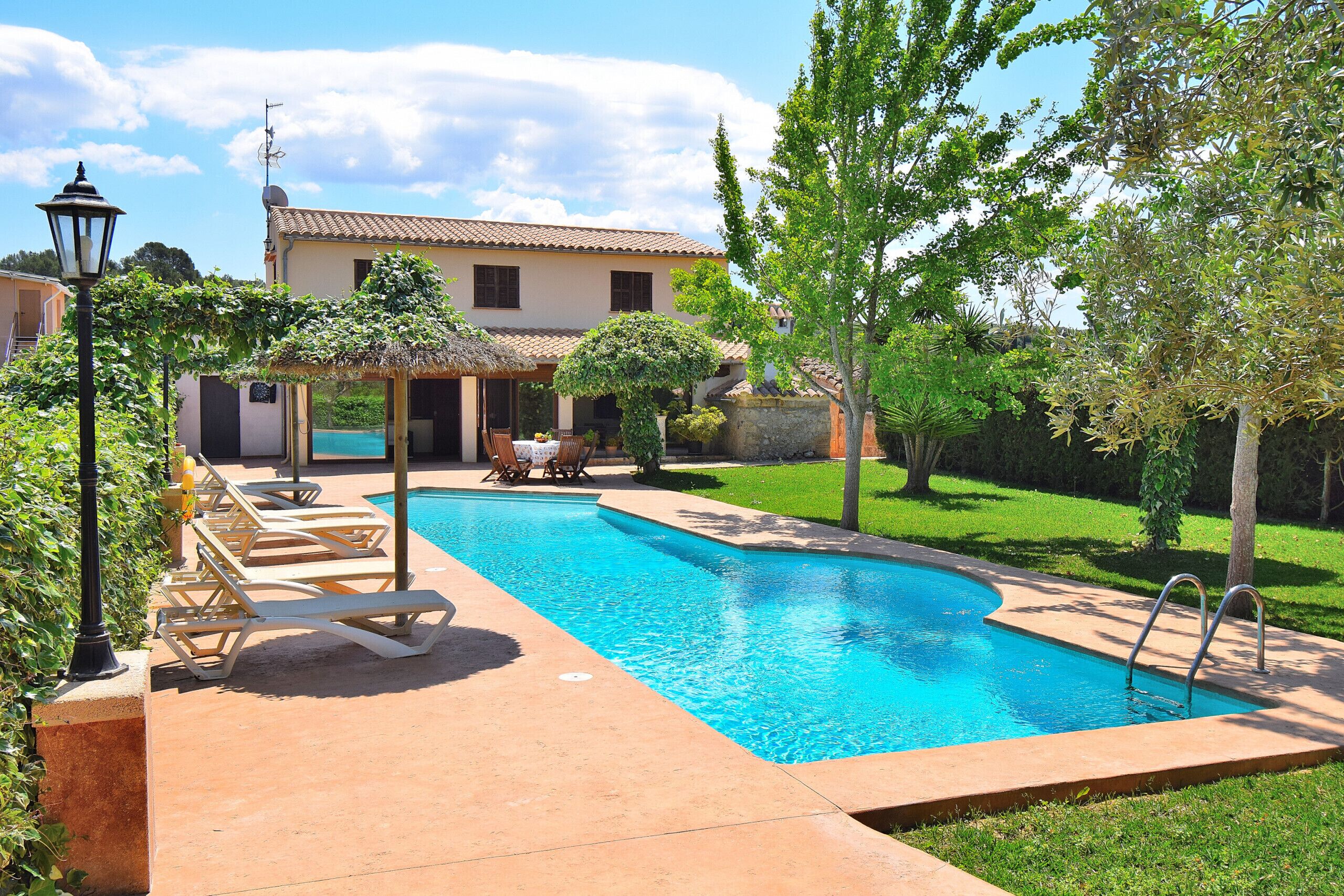 A swimming pool with lounge chairs, a pergola, and a house in the background.